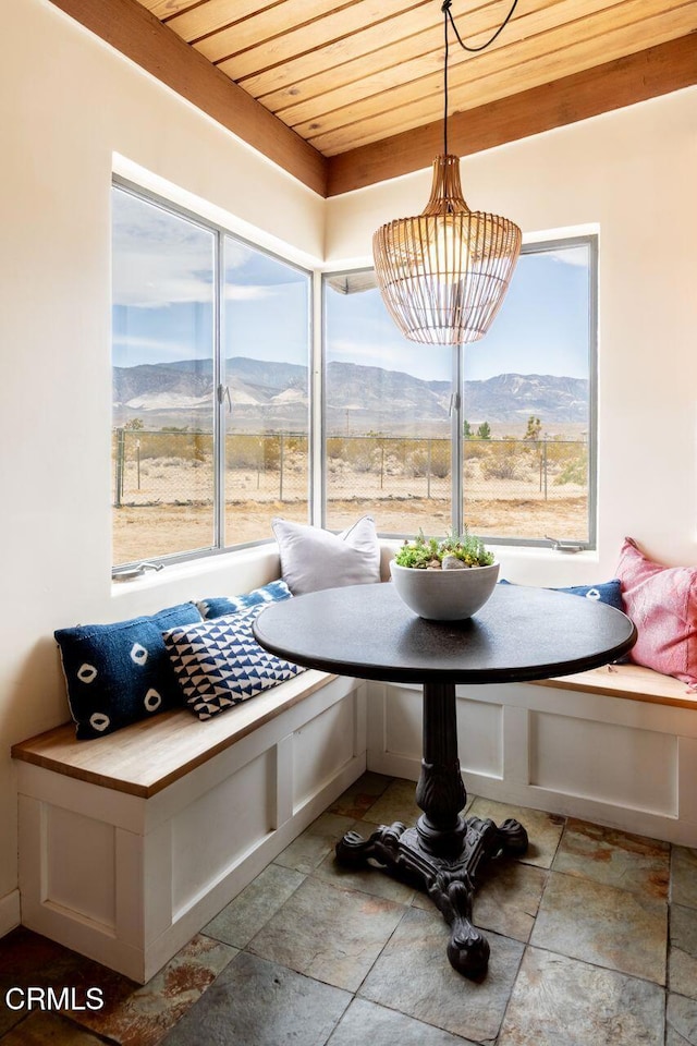 dining space with breakfast area, stone tile floors, wooden ceiling, a mountain view, and healthy amount of natural light