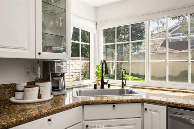 kitchen with a sink, stainless steel dishwasher, white cabinetry, and glass insert cabinets