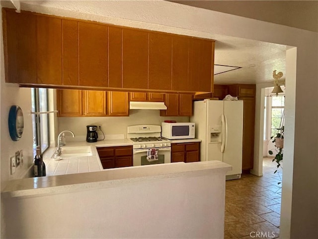 kitchen with white appliances, a sink, under cabinet range hood, a peninsula, and light countertops