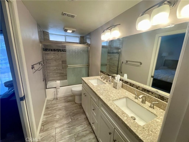 ensuite bathroom with double vanity, toilet, enclosed tub / shower combo, and baseboards