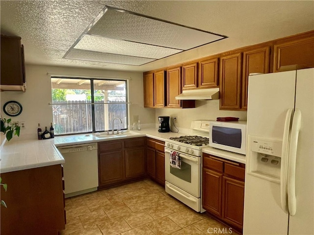 kitchen featuring white appliances, a sink, under cabinet range hood, brown cabinetry, and light countertops