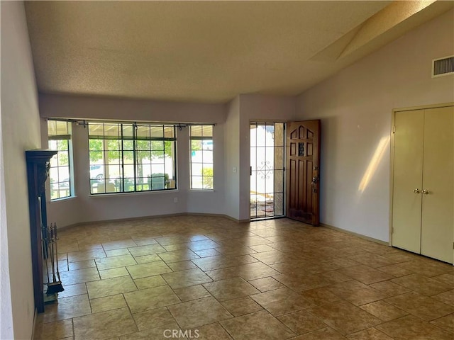 empty room with healthy amount of natural light, baseboards, stone tile flooring, and vaulted ceiling