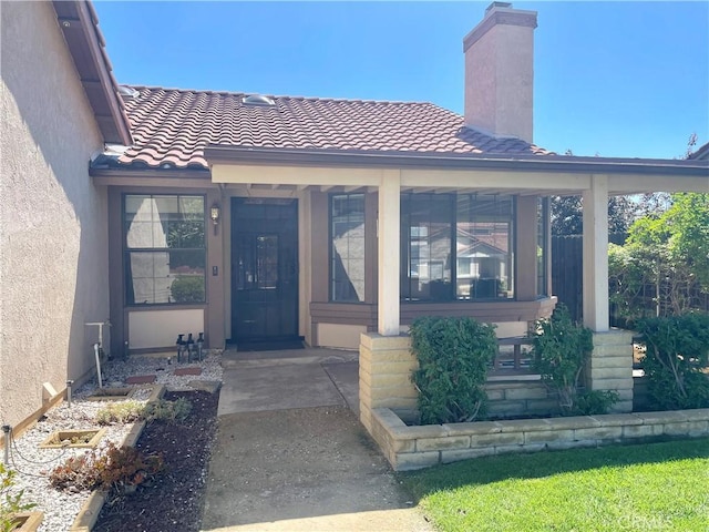 view of exterior entry with a chimney, a tile roof, and stucco siding