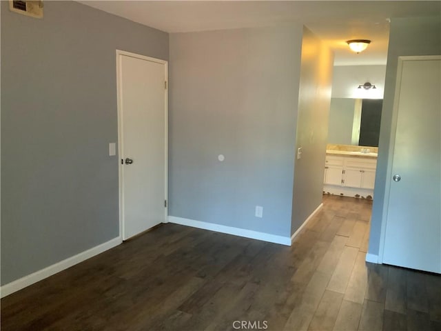 unfurnished bedroom with dark wood-type flooring, baseboards, and ensuite bathroom