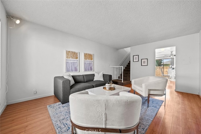 living room featuring stairs, a textured ceiling, light wood-style floors, and baseboards