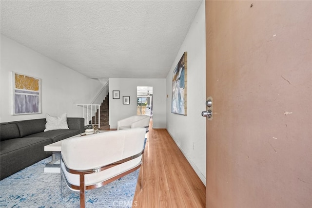 living room with stairs, light wood-style flooring, a textured ceiling, and baseboards