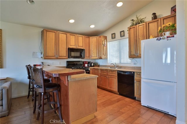 kitchen with black appliances, a peninsula, a breakfast bar, light wood-type flooring, and a sink