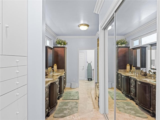 bathroom featuring two vanities, crown molding, baseboards, and marble finish floors