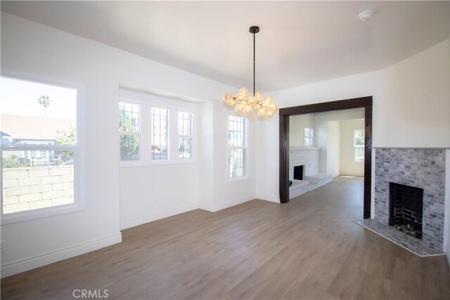 unfurnished dining area with a brick fireplace, a chandelier, wood finished floors, and baseboards