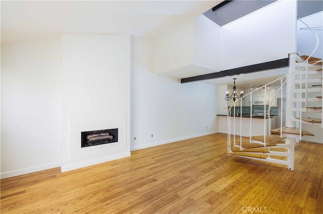 2900 Madison Ave Unit D16, Fullerton, CA 92831 - unfurnished living room with a chandelier, wood finished floors, stairway, baseboards, and a high ceiling