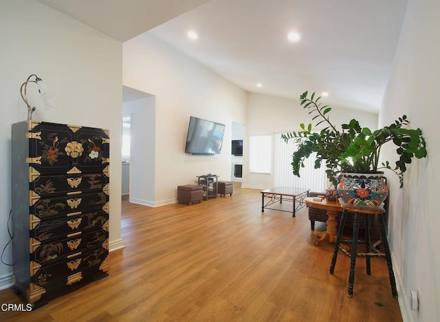 living area featuring vaulted ceiling, wood finished floors, recessed lighting, baseboards, and healthy amount of natural light