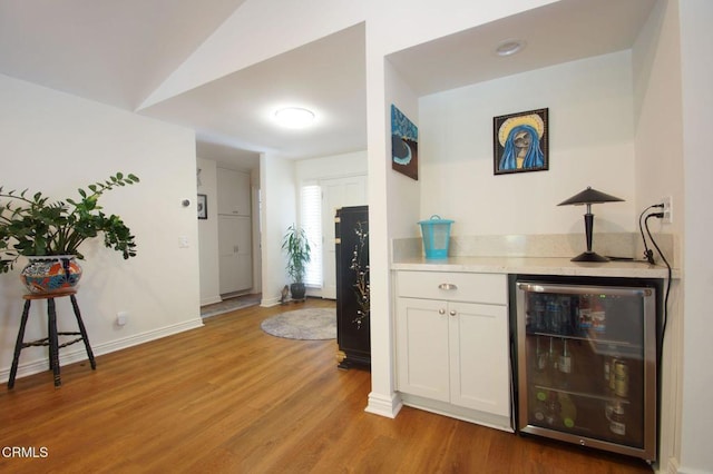 indoor dry bar with beverage cooler, light wood-style floors, baseboards, and lofted ceiling