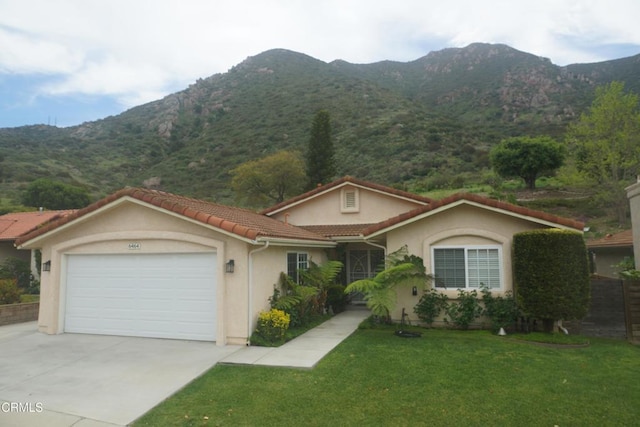 view of front of property featuring a mountain view, concrete driveway, an attached garage, and a front yard