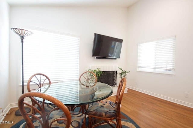 dining room featuring baseboards, wood finished floors, and a fireplace with raised hearth