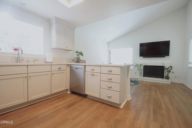 kitchen with dishwasher, a sink, a peninsula, light wood-style floors, and lofted ceiling