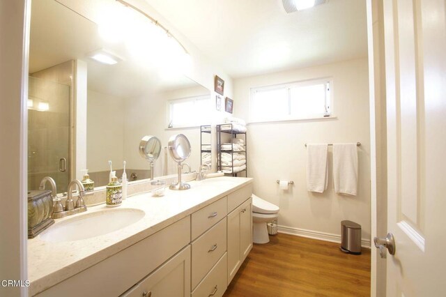 full bath featuring baseboards, a stall shower, toilet, wood finished floors, and double vanity