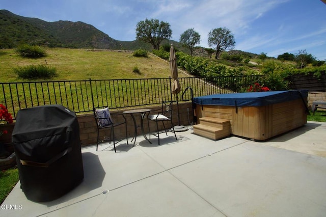 view of patio with a hot tub, fence, a mountain view, and grilling area