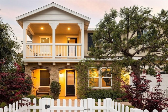 view of front of house with a balcony, a fenced front yard, a gate, covered porch, and stone siding