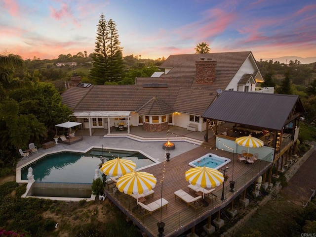 back of house with an in-ground hot tub, a gazebo, outdoor dining space, a wooden deck, and an outdoor pool