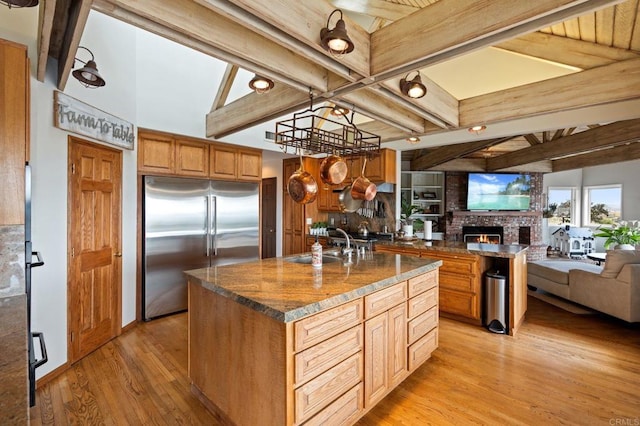 kitchen with stainless steel built in fridge, open floor plan, light wood finished floors, a sink, and beam ceiling