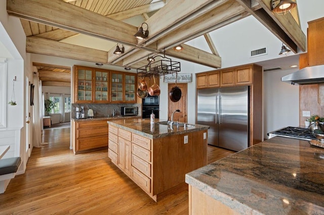 kitchen featuring black appliances, a sink, light wood finished floors, under cabinet range hood, and tasteful backsplash
