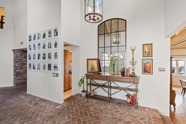 foyer with brick floors, a high ceiling, a chandelier, and baseboards