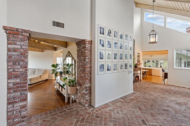 corridor with brick flooring, a high ceiling, a chandelier, beamed ceiling, and baseboards