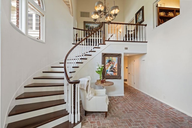 stairs with a chandelier, brick flooring, baseboards, and a high ceiling
