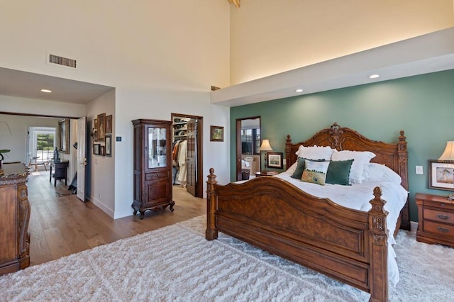 bedroom with light wood-style flooring, baseboards, recessed lighting, a spacious closet, and a towering ceiling