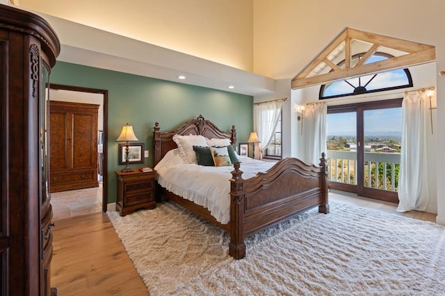 bedroom featuring access to exterior, light wood-style floors, a towering ceiling, and baseboards