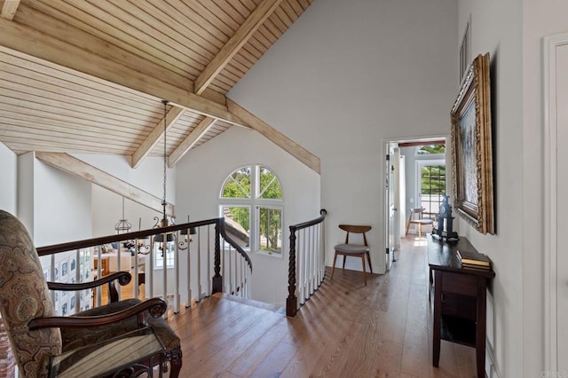 hall featuring an upstairs landing, plenty of natural light, hardwood / wood-style floors, beamed ceiling, and a chandelier
