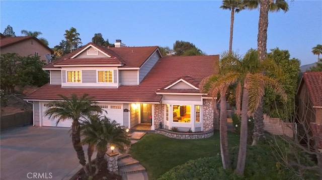 traditional-style home with concrete driveway, a garage, a front yard, a chimney, and stone siding