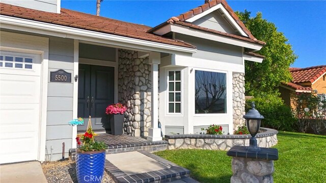 property entrance featuring covered porch, stone siding, a tiled roof, and a yard