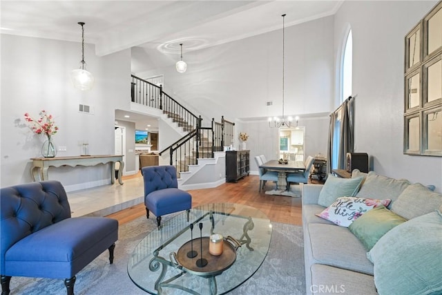 living room with a towering ceiling, a chandelier, stairs, wood finished floors, and baseboards