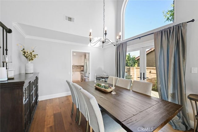 dining space with a chandelier, crown molding, dark wood-style floors, french doors, and a high ceiling