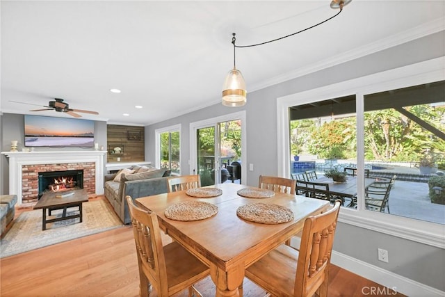 dining area with light wood-type flooring, ceiling fan, a brick fireplace, baseboards, and ornamental molding