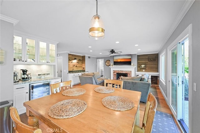 dining room with crown molding, a brick fireplace, recessed lighting, wine cooler, and wood finished floors