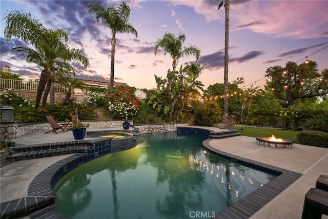 pool at dusk with an outdoor fire pit, a patio, and a pool with connected hot tub