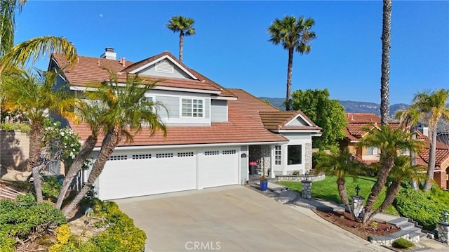 traditional-style home featuring concrete driveway, a tiled roof, a front lawn, and an attached garage