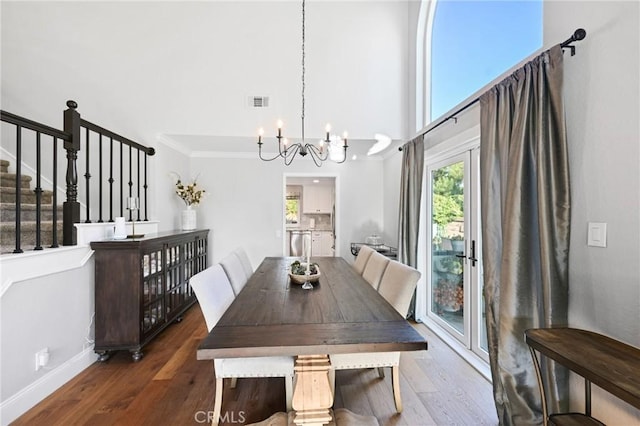 dining space featuring a chandelier, a towering ceiling, wood finished floors, stairs, and baseboards