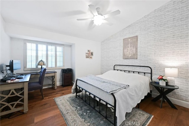 bedroom featuring lofted ceiling, brick wall, a desk, wood finished floors, and baseboards