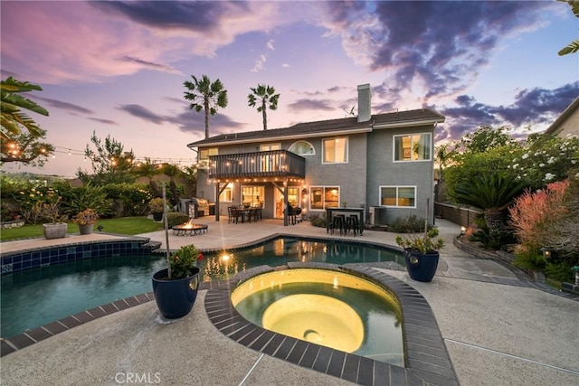 pool at dusk featuring a patio area, a pool with connected hot tub, outdoor dining space, an outdoor fire pit, and a deck