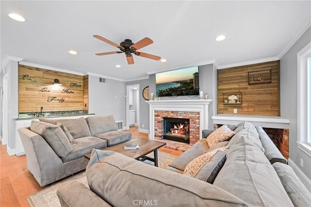 living room featuring wooden walls, ceiling fan, a fireplace, crown molding, and recessed lighting
