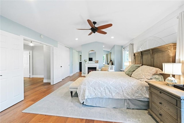 bedroom with wood finished floors, a fireplace, vaulted ceiling, baseboards, and recessed lighting