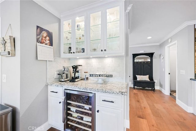 indoor bar featuring wine cooler, ornamental molding, backsplash, baseboards, and light wood-style flooring
