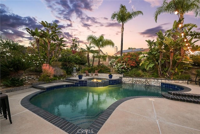 pool at dusk with a pool with connected hot tub and a patio