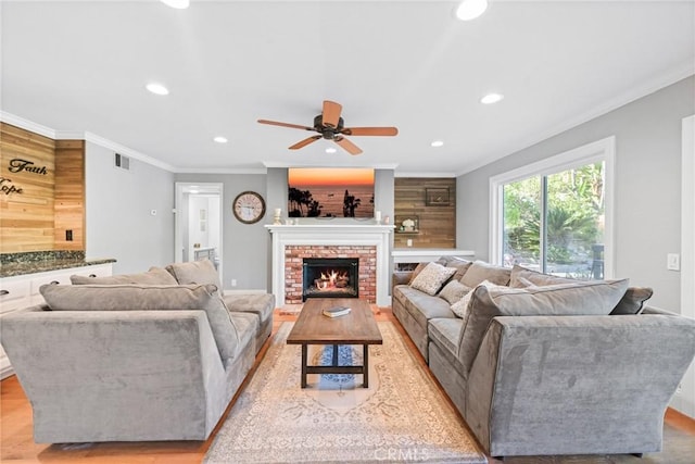 living area with recessed lighting, a ceiling fan, crown molding, light wood-style flooring, and a brick fireplace