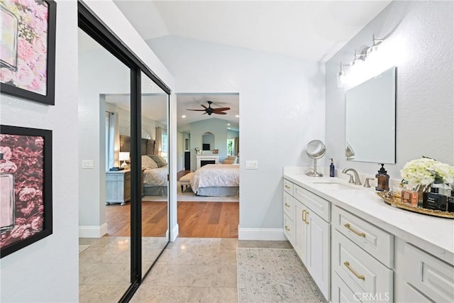 ensuite bathroom with lofted ceiling, a fireplace, ceiling fan, vanity, and baseboards