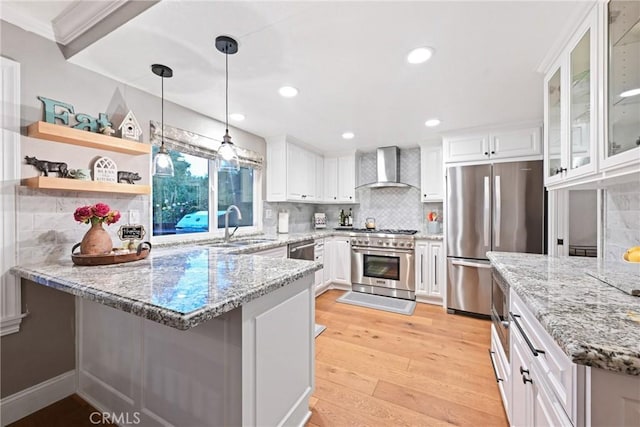 kitchen with appliances with stainless steel finishes, wall chimney range hood, a peninsula, light wood-style floors, and white cabinets