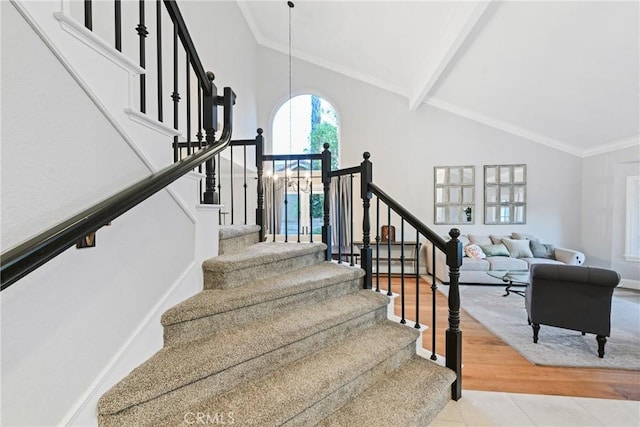stairs with high vaulted ceiling, wood finished floors, beamed ceiling, ornamental molding, and baseboards